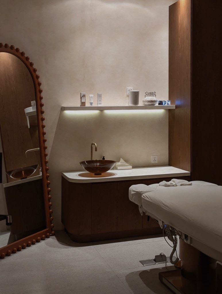 Treatment room with a bed, basin and arched mirror at Mello Spa Canggu