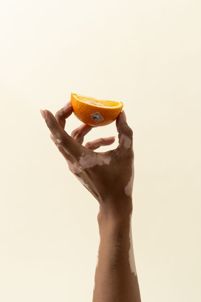A hand holding up a slice of orange against a soft cream background