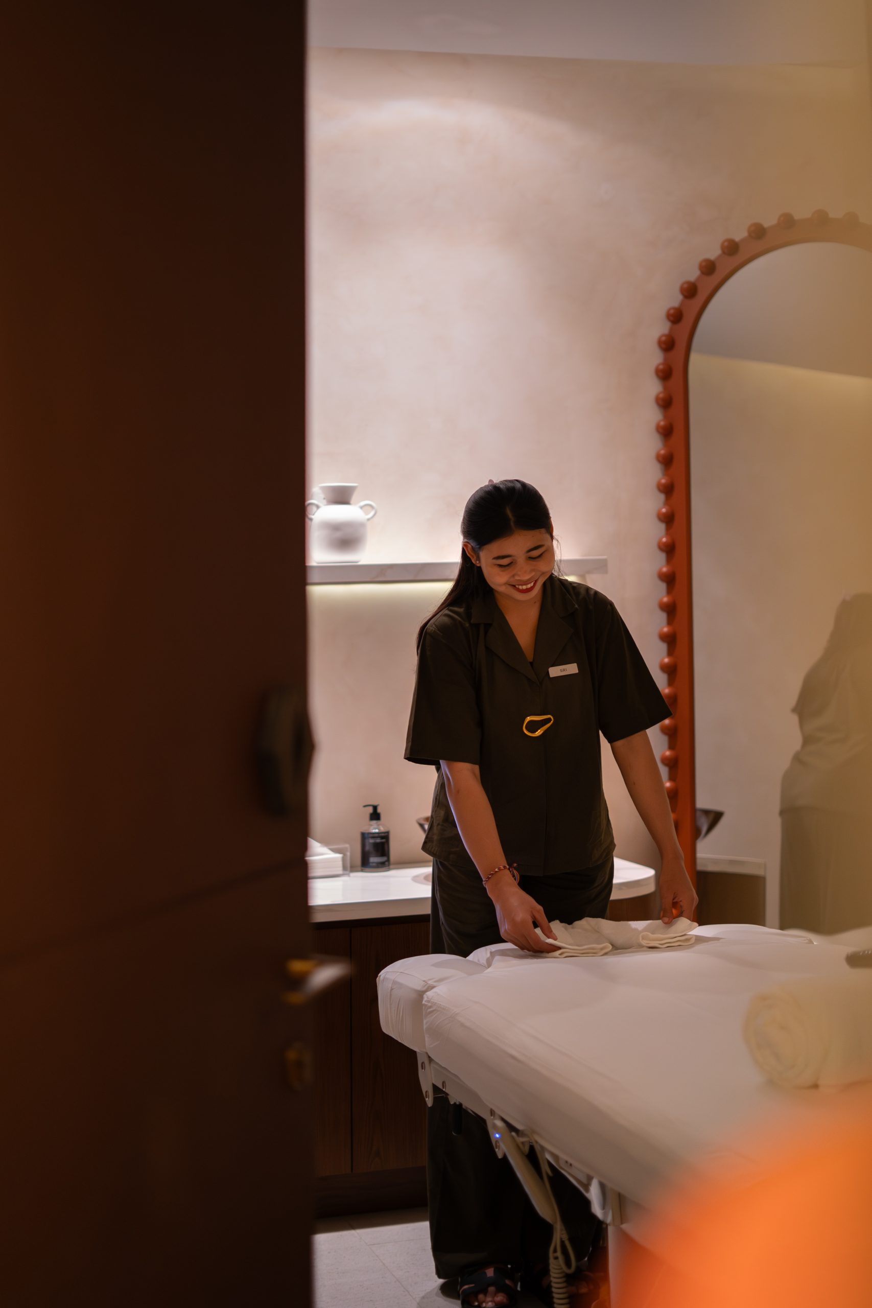 Therapist at Mello Spa Canggu preparing a treatment bed beside the scalloped arch mirror