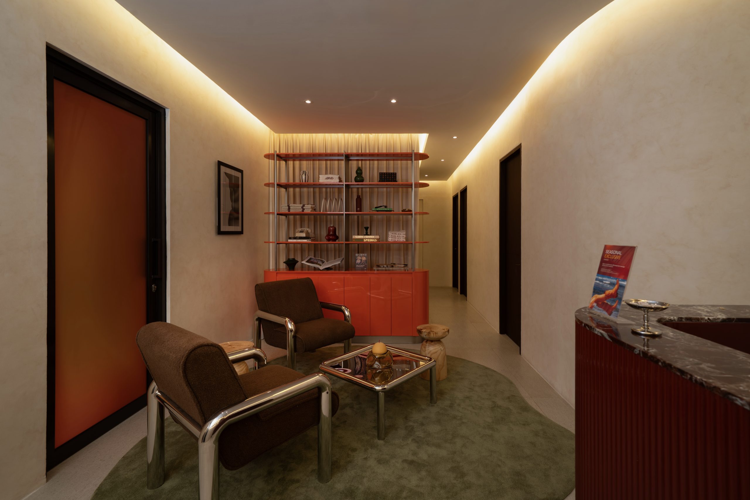 Reception lounge at Mello Spa Canggu with brown boucle armchairs, open shelving and a red fluted desk